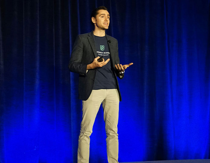 Man speaking on stage, wearing blazer and casual clothes, in a presentation about TikTok moms and disliked professions.
