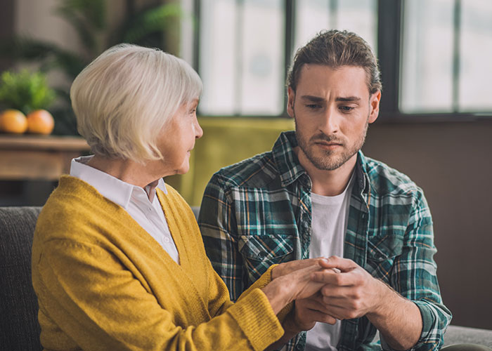 Mother and adult son having a serious conversation indoors, illustrating a mom admitting she hid college acceptance letters. Mother and adult son having a serious conversation indoors, illustrating a mom admitting she hid college acceptance letters.