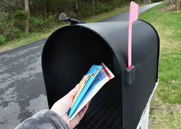 Hand pulling mail, including college acceptance letters, from an open black mailbox with a red flag raised on a rural road. Hand pulling mail, including college acceptance letters, from an open black mailbox with a red flag raised on a rural road.