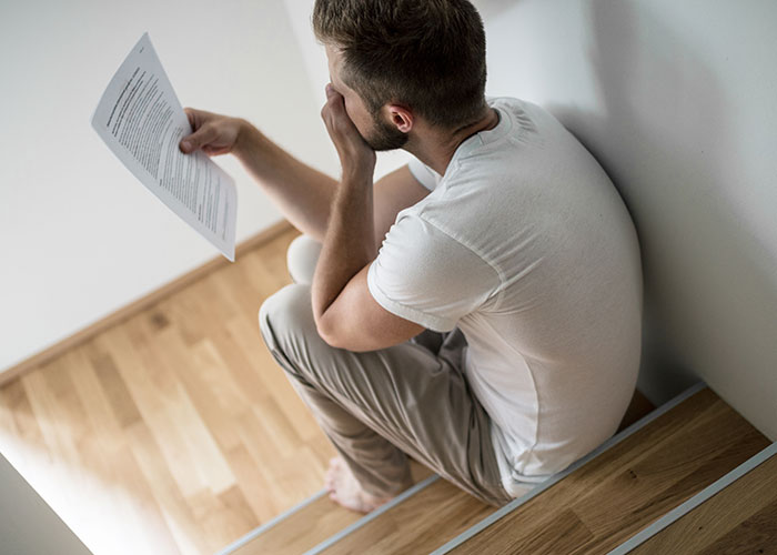 Young man sitting on stairs holding a letter, appearing upset about college acceptance and hidden news from mom. Young man sitting on stairs holding a letter, appearing upset about college acceptance and hidden news from mom.
