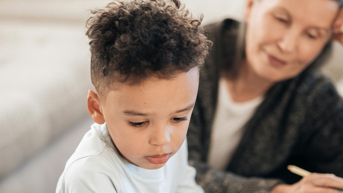 Young grandchild looking down thoughtfully as his grandmother watches nearby, hinting at inheritance tensions
