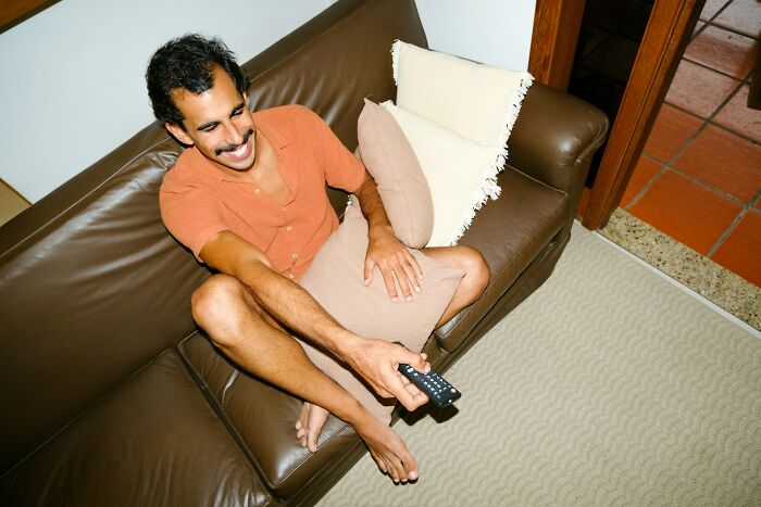 Man lounging on a couch holding a remote, illustrating adults who somehow failed to understand growing up is mandatory.