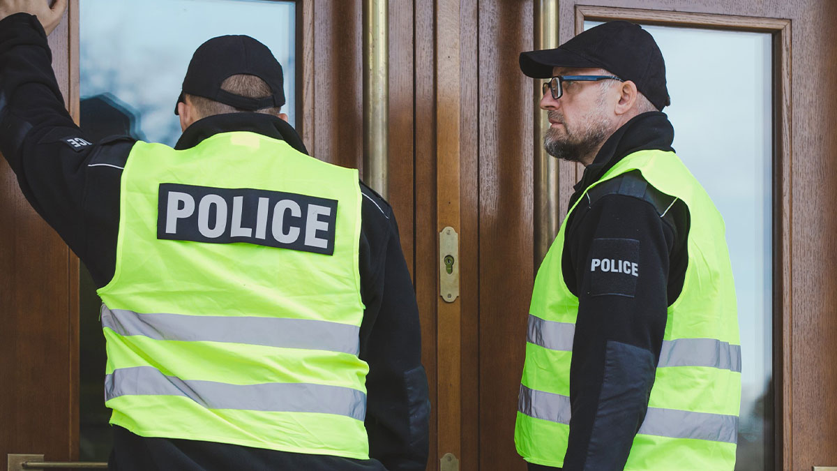 Two police officers in yellow vests at a wooden door, illustrating innocent people blamed by police situations.