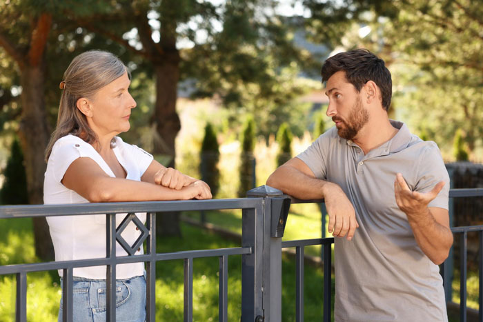 Neighbor upset talking with man over nanny parking issue in front of home near a metal gate on a sunny day Neighbor upset talking with man over nanny parking issue in front of home near a metal gate on a sunny day