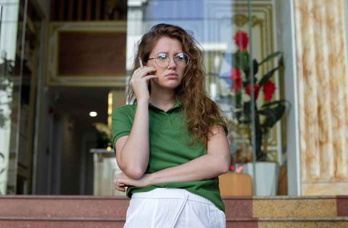 Young woman upset on phone standing outside home, representing neighbor upset over nanny parking in front of house Young woman upset on phone standing outside home, representing neighbor upset over nanny parking in front of house