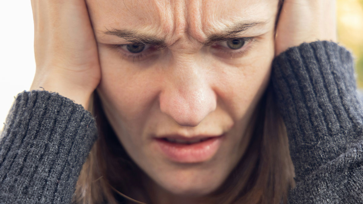 Woman with a distressed expression covering her ears, illustrating curiosity and neighbor spying concerns.
