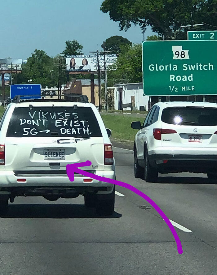 White car with false scientific claims about viruses and 5G on the rear window, highlighting absurd scientific takes in society.