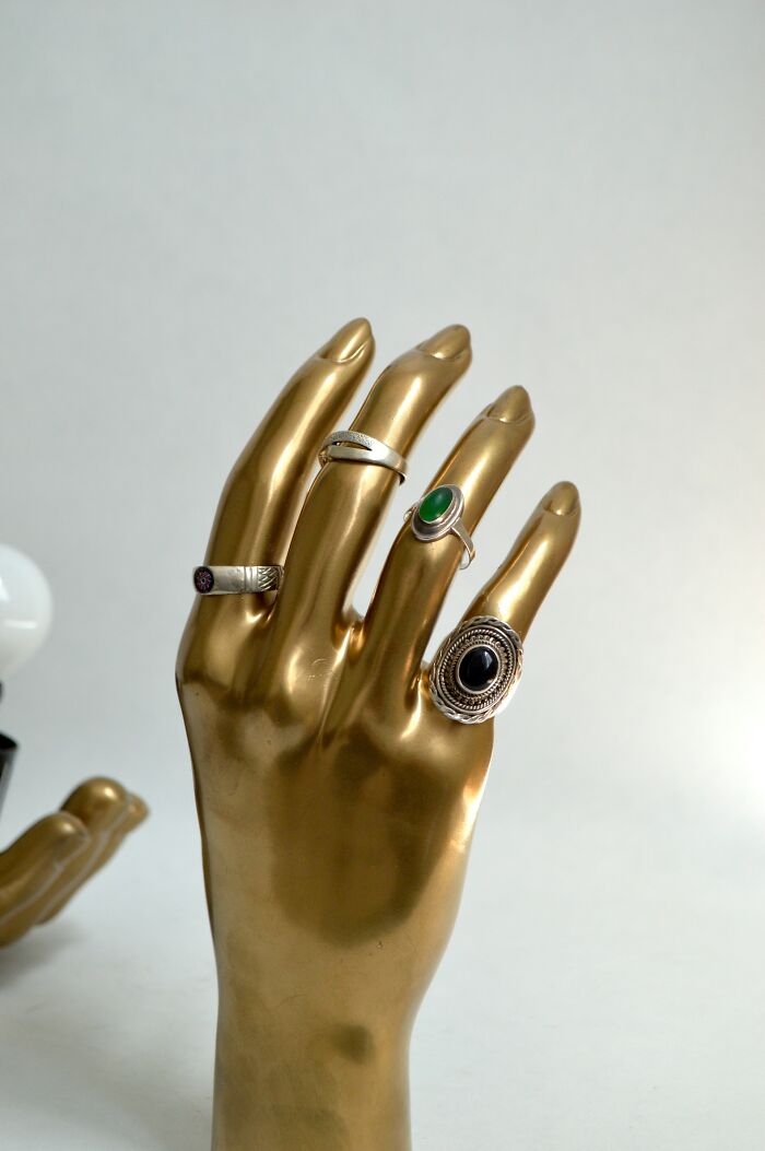 Golden hand display with silver rings featuring green and black stones, evoking creepy stories to tell in dark woods atmosphere. Golden hand display with silver rings featuring green and black stones, evoking creepy stories to tell in dark woods atmosphere.