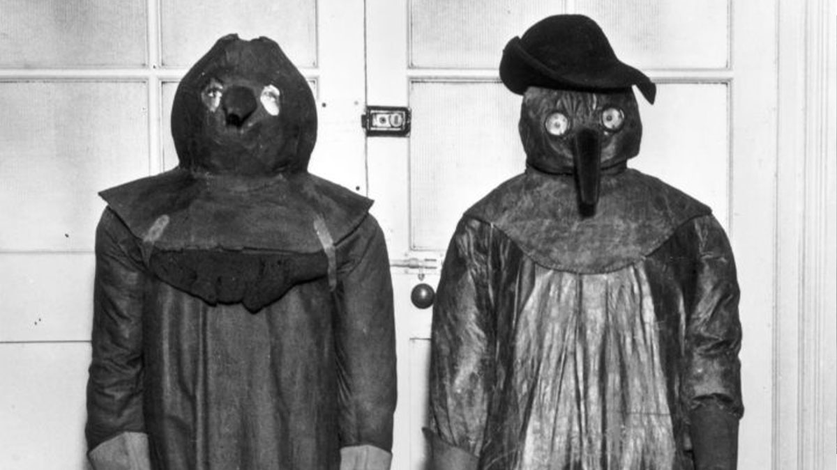 Two people wearing old-school medical plague doctor costumes with bird-like masks and protective gowns.