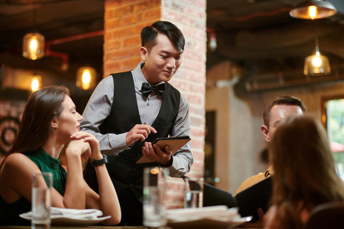 Waiter taking an order from diners in a restaurant, focusing on ordering fried pork intestine menu options. Waiter taking an order from diners in a restaurant, focusing on ordering fried pork intestine menu options.