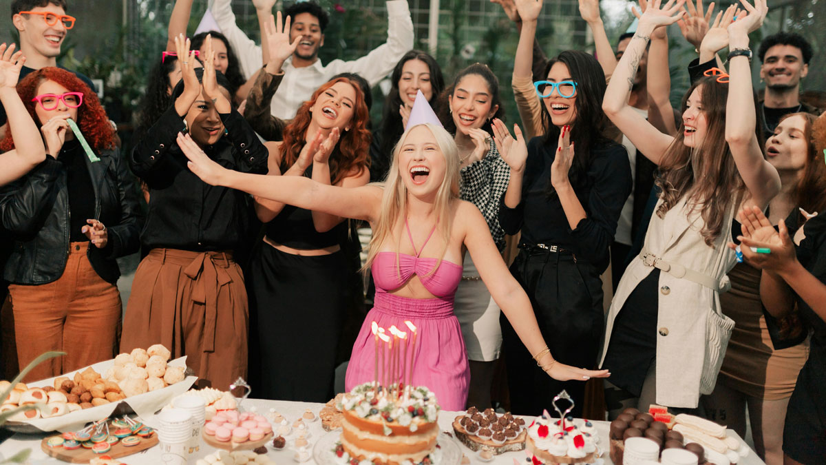 Teen celebrating 18th birthday surrounded by friends with cakes and desserts, showing happiness despite gift disappointment.