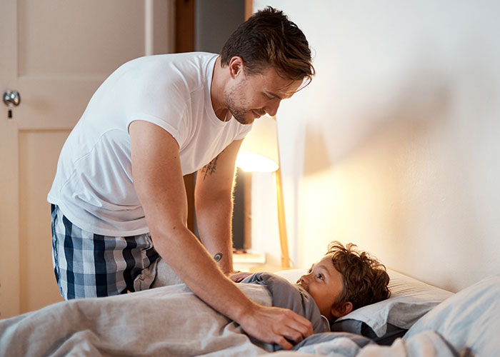 A young man tenderly tucking his younger sibling into bed, highlighting family responsibilities and care.