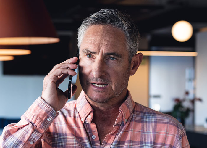 Middle-aged man in plaid shirt talking on phone, reflecting on being made to raise his younger siblings by parents.