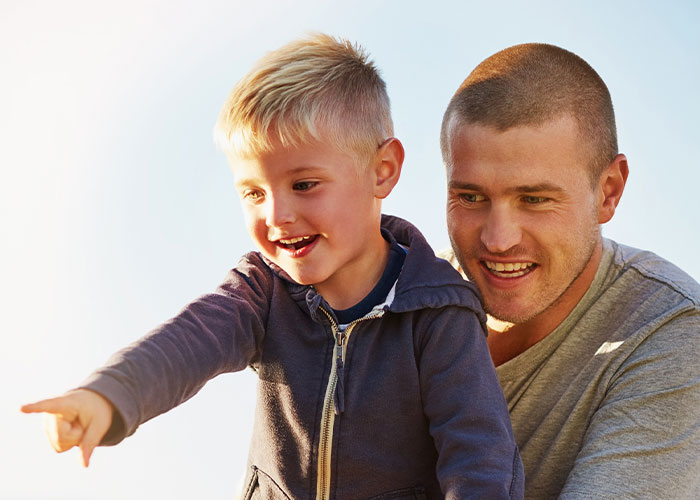 Young boy happily pointing while being supported by an adult male, illustrating siblings and family responsibility themes.