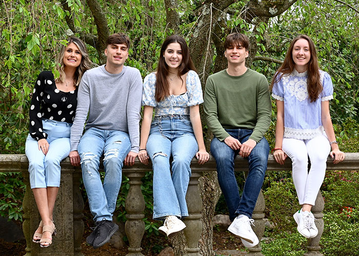 Five smiling young adults sitting outdoors, representing siblings involved in a story about family and responsibility.