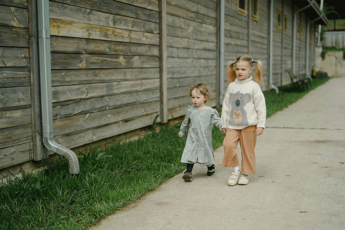 Two young sisters walking outside along a wooden fence, depicting forced parenting of little sister by 19YO sibling. Two young sisters walking outside along a wooden fence, depicting forced parenting of little sister by 19YO sibling.