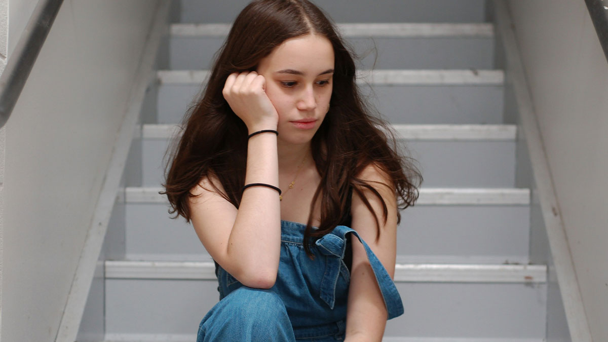 19YO girl looking upset while sitting on stairs, symbolizing forced parental role for her little sister frustrations