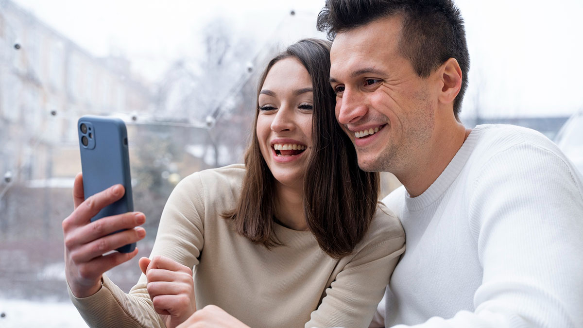 A couple smiling and taking a selfie with a partner phone unhinged thing in a bright indoor setting.
