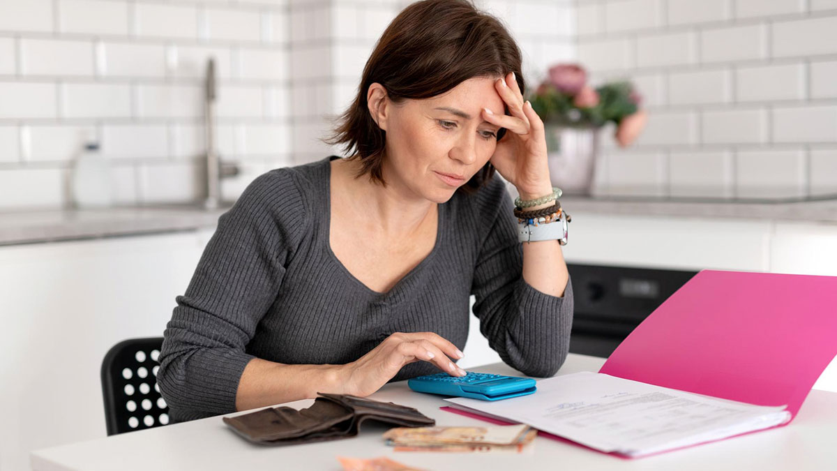 Woman calculating finances with a calculator and documents, concerned about paying off daughter student loans at home.