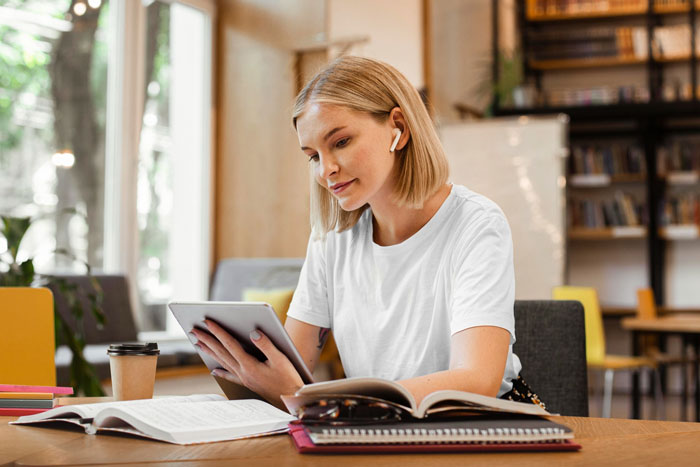 Young woman focused on tablet with books open, studying in a cozy space related to paying off daughter student loans. Young woman focused on tablet with books open, studying in a cozy space related to paying off daughter student loans.