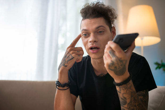 Young man with tattoos holding smartphone, thinking deeply about paying off daughter student loans at home. Young man with tattoos holding smartphone, thinking deeply about paying off daughter student loans at home.