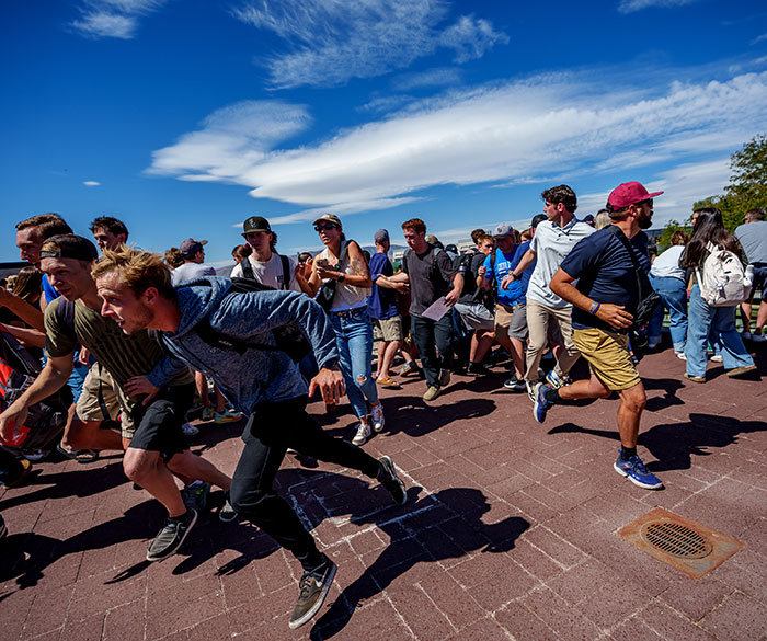 Crowd of people running outdoors under a blue sky, illustrating witnesses describing last moments as manhunt for culprit continues. Crowd of people running outdoors under a blue sky, illustrating witnesses describing last moments as manhunt for culprit continues.