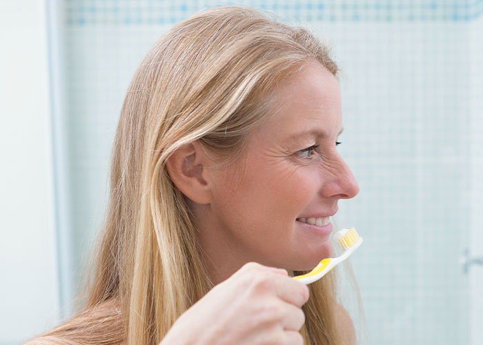 Woman smiling and holding a toothbrush in a bathroom demonstrating a simple life hack that actually works.