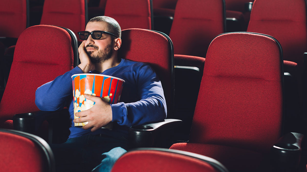 Man in 3D glasses sitting alone in theater holding popcorn, illustrating clever life hacks that actually work.