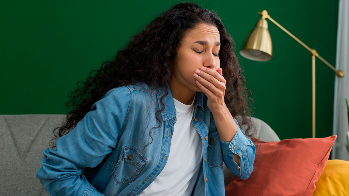 Woman covering her mouth feeling sick, possibly poisoned, sitting on a couch with concerns about suspicious behavior from MIL.