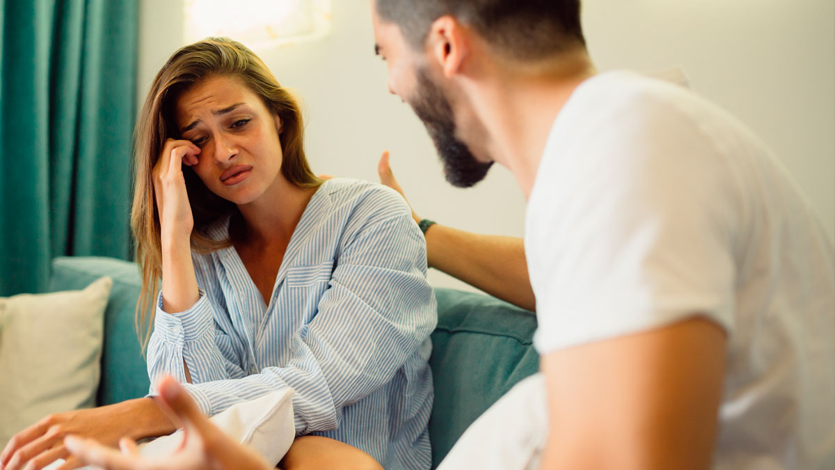 Upset woman and man having tense conversation on sofa, depicting family rejection and fiancu00e9u2019s earnings revealed.