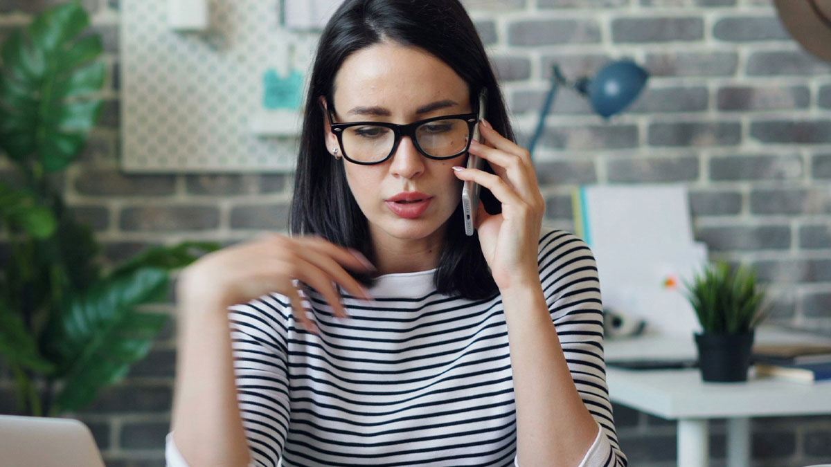 Young personal assistant in glasses speaking on phone while working in a modern home office environment focused on billionaires.