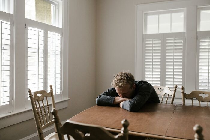 A man sitting alone at a wooden table in a bright room, reflecting on life after pressured marriage decisions.