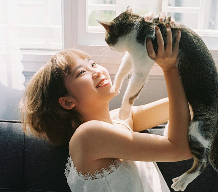 Young woman joyfully holding her cat indoors, highlighting parents trying to get rid of her cat while pregnant sister visits. Young woman joyfully holding her cat indoors, highlighting parents trying to get rid of her cat while pregnant sister visits.