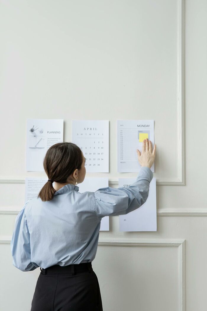 Woman organizing planning and calendar sheets on a white wall, illustrating challenges women face compared to men freely.