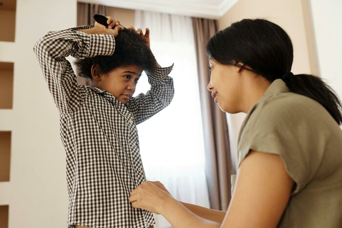 Parent helping child with hair in a bright room, illustrating parenting hacks that save sanity in daily routines.