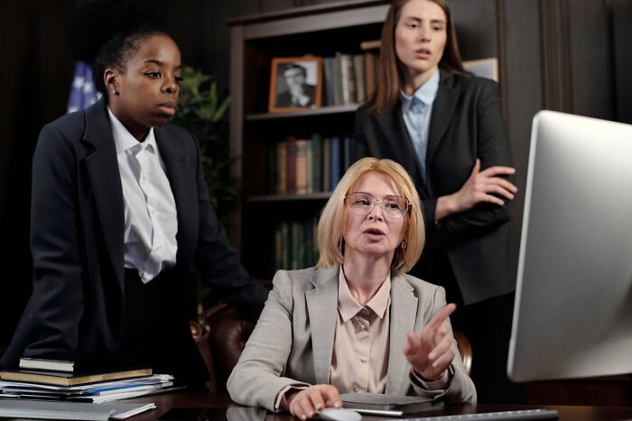 Three professional women working together at a desk, highlighting gender roles and things women are not allowed to do compared to men.