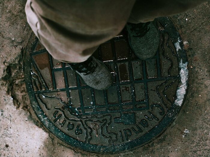 Person standing on an old manhole cover, representing terrifying true stories from people who explore beneath our feet.