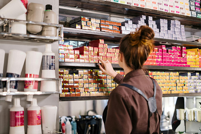 Woman selecting box dye from salon shelves filled with colorful hair dye boxes and beauty products on display Woman selecting box dye from salon shelves filled with colorful hair dye boxes and beauty products on display