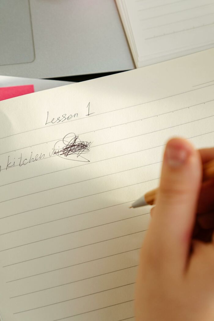 Close-up of a hand holding a pencil over a notebook with scribbled notes about lesson one tattoo ideas.