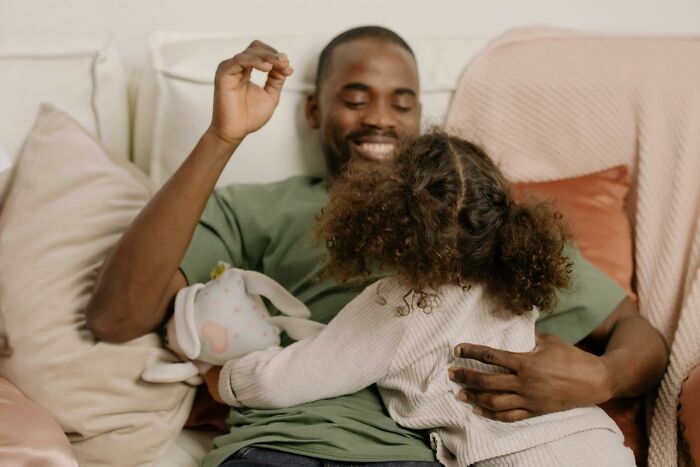 Father and daughter sharing a joyful moment on a couch, illustrating parenting hacks that save sanity and bring happiness.