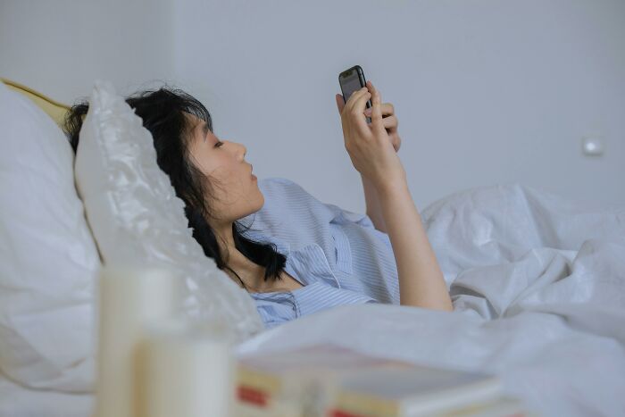 Woman lying in bed looking at her phone, reflecting on nasty things exes did that shocked and grossed out partners.
