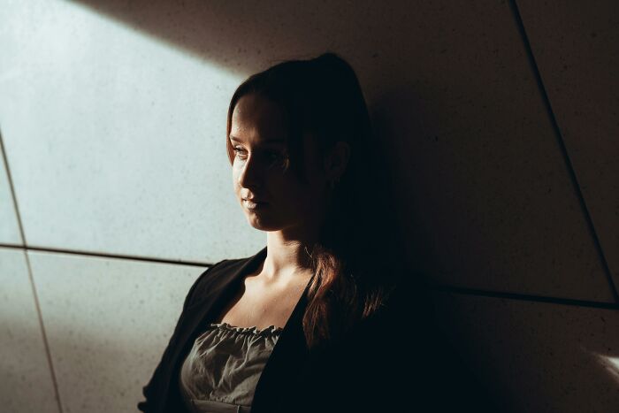 Woman in shadowed room looking thoughtful and upset, illustrating partner shock and grossed out by nasty ex behaviors.
