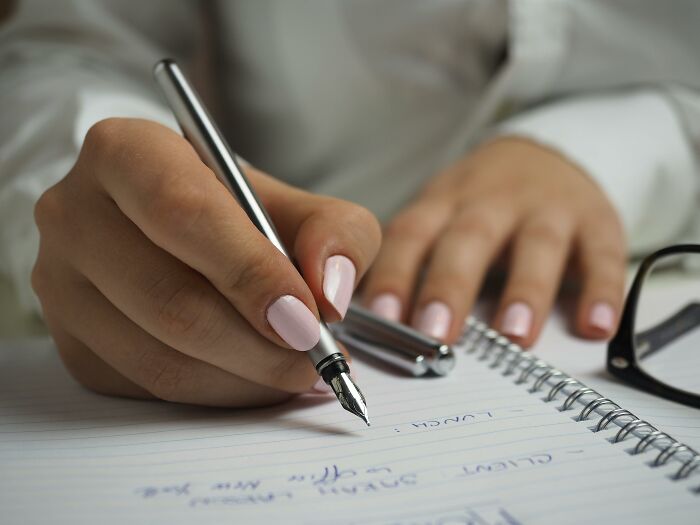 Person writing with a silver pen in a notebook, illustrating things people used to spend hours doing pointlessly.