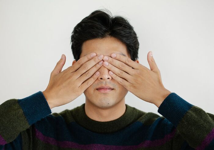Man covering his eyes with hands, symbolizing hesitation about tattoo choices and clients’ worst tattoo requests.
