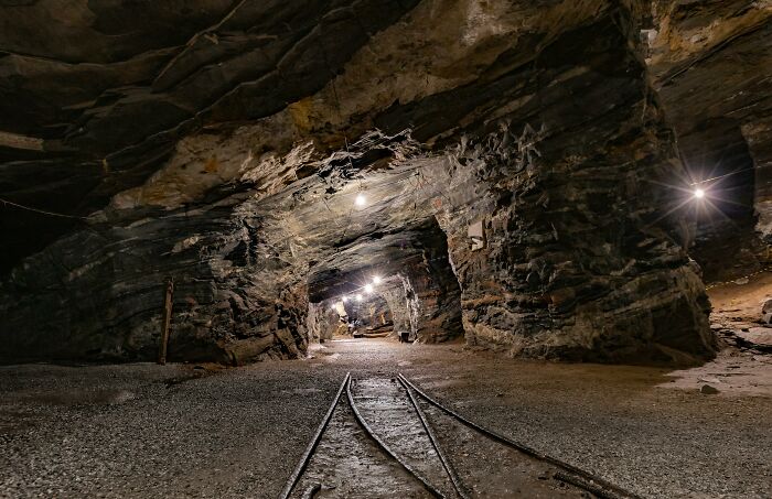 Underground mining tunnel with dim lights and tracks, showing the environment where people work and explore beneath our feet.