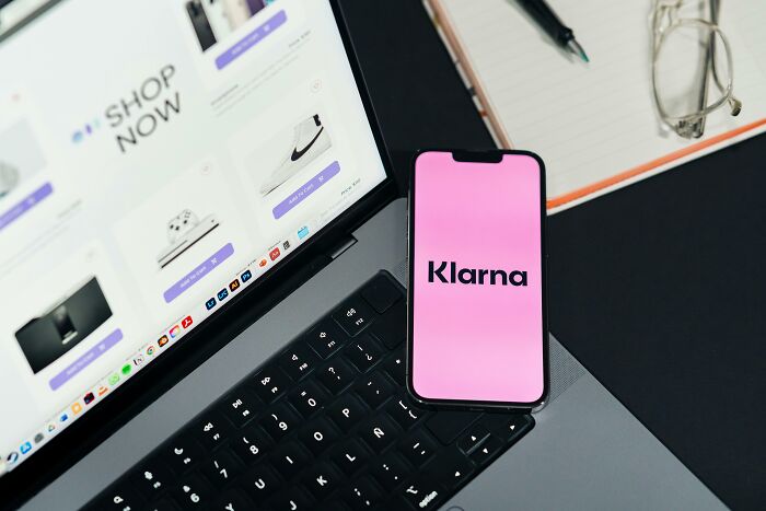 Smartphone showing Klarna app on laptop keyboard with online shopping page open, highlighting overhyped products concept.