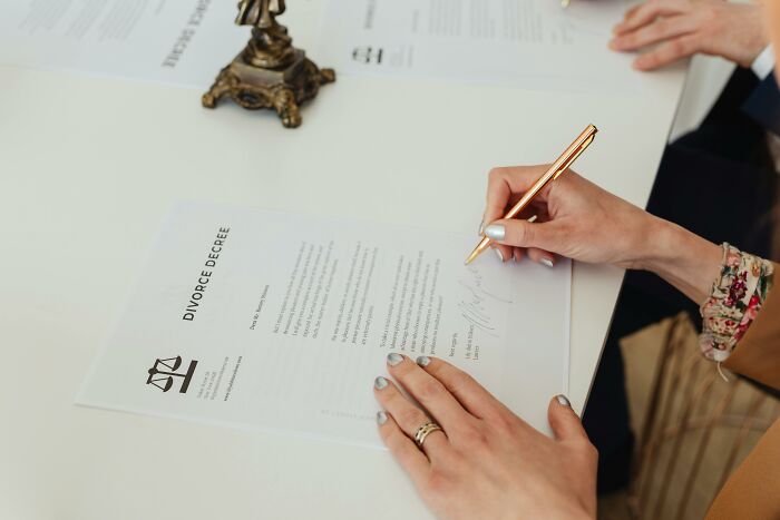 Close-up of a woman signing a divorce decree, representing life updates of men who married under pressure.
