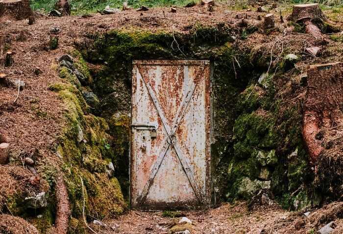 Rusty metal door embedded in a mossy hillside, representing terrifying true stories from people who work and explore beneath our feet.