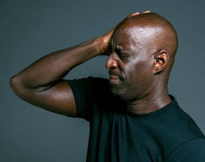 Man in black shirt holding head with painful expression, illustrating real-life hexes and odd curses belief in witchcraft.