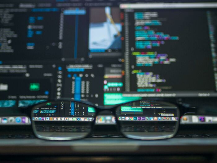 Close-up of glasses focusing on computer screens filled with coding, illustrating things people used to spend hours doing.